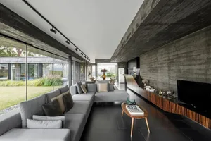 A modern living room with concrete walls, large windows, and a comfortable sectional sofa.