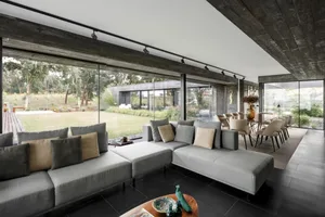 Modern minimalist living room featuring concrete and glass materials, with large windows and a spacious layout.