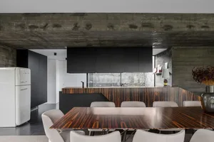 A modern kitchen dining space featuring black concrete ceiling and black wooden cabinets with a white dining table and chairs
