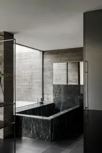 Modern minimalist bathroom with black marble tub and concrete walls.