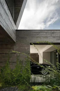 A modern residential building with a minimalist design, featuring a concrete exterior and an open-air carport.