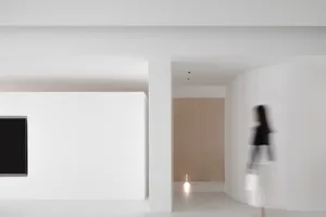 A minimalist white corridor with soft lighting and a person blurred in motion.