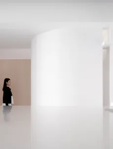 A minimalist white interior space featuring a curved white wall and a person standing in the foreground.