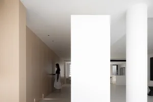 A modern minimalist corridor with white walls and wooden panels, featuring a person walking.