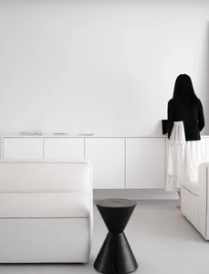 A minimalist living room featuring white furniture and a black accent table.
