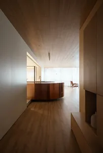 A minimalist interior design featuring a wooden kitchen island and floor, with white walls and large windows.