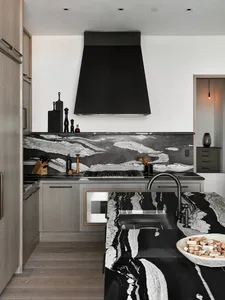 Modern kitchen with a marble countertop and backsplash, featuring a black hood and wooden floor.