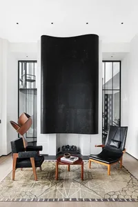A modern living room with a black, wall-mounted fireplace, black leather armchairs, a round wooden coffee table, and a patter