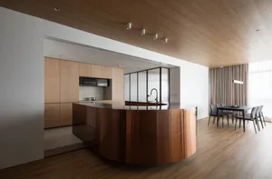 Modern minimalist kitchen featuring wooden cabinets and a curved black countertop, illuminated by recessed lighting in a spac