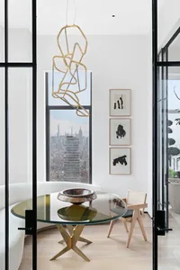 A modern minimalist living room with a glass table, metal chandelier, wooden chair, and steel accents, featuring a cityscape 