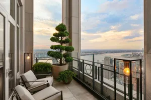 Modern terrace with concrete patio, floor-to-ceiling glass walls, potted plants, and warm lighting at sunset overlooking a ci