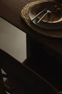 An industrial dining table setting featuring a metal plate with a knife and fork on a woven place mat.