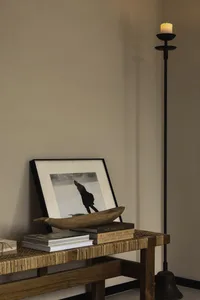 A candlestick with a wooden bowl, books, and a framed black-and-white photograph on a woven bench in an industrial-style livi