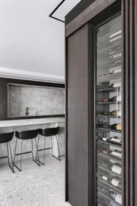 Modern kitchen bar with concrete countertop, black stools, and a glass-fronted wine cabinet.