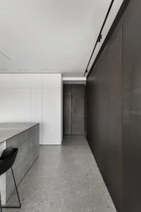 A modern minimalist kitchen with a concrete countertop, white and dark wood cabinets, and black stools.