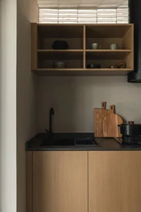 Modern kitchen with open shelving and wooden cabinets, featuring ceramic cups and wooden cutting board.