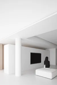 A sleek, minimalist living room with concrete walls, white furniture, and a black television mounted on the wall.