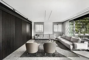 Modern minimalist living room featuring concrete flooring, gray sofas, and a blackwood stripped wall.
