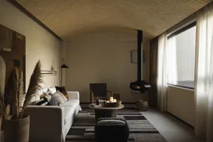 A minimalist living room with a white sofa, black coffee table, and a hanging fireplace, featuring neutral tones and natural