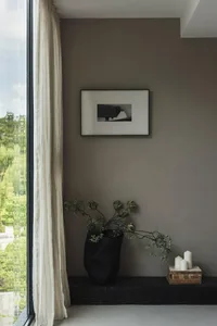 Minimalist interior design featuring a window corner with concrete wall and floor, framed picture, and decorative vase.