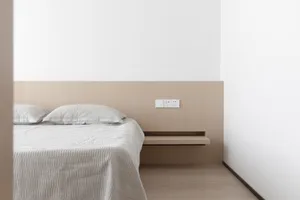 簡約臥室內擺放白色床鋪，搭配硬木地板、簡約木質床頭板與懸浮式床頭櫃。