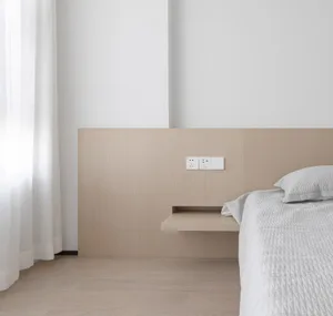 A minimalist bedroom featuring a floating wood shelf next to the bed and a white curtain.