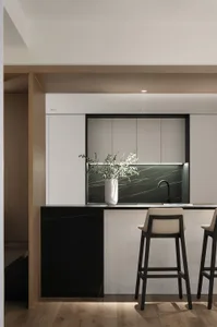 Modern minimalist kitchen with marble backsplash, bar stools, and sleek white cabinets.