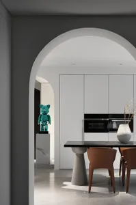Modern kitchen featuring sleek white cabinets, black countertops, and a shiny green glass sculpture on a pedestal.