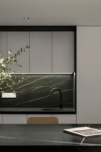 A modern minimalist kitchen features a marble backsplash and countertop with a black faucet and a plant.