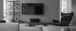Modern living room featuring industrial decor with concrete walls, black armchair, and a grey sofa with throw blankets.