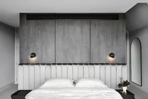 A minimalist bedroom with a wooden headboard and white bedding, featuring grey walls and a mirrored accent wall.