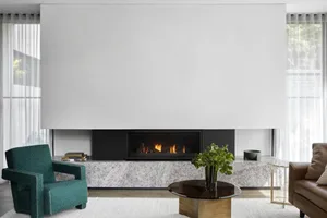Modern minimalist living room featuring a large fireplace with a marble hearth and a white wall above it, with a small green 