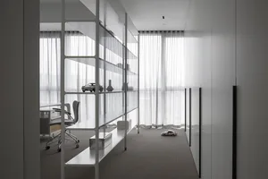 A minimalist office interior with glass shelving, a desk, and a chair.