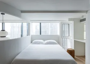 A minimalist white bedroom with large windows overlooking a cityscape.