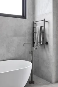 A modern bathroom with a white freestanding bathtub, a towel rack with a towel, and a window.