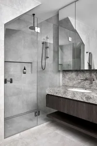 Modern bathroom with concrete walls, marble vanity, and glass shower enclosure.