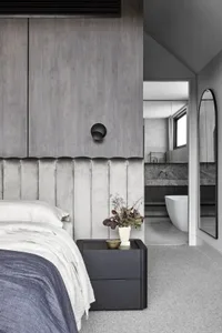 A modern bedroom featuring a gray wall with a textured pattern, a bed with white bedding, and a dark nightstand with a plant.