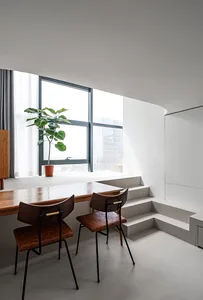 Modern dining room with concrete floor, wooden table, and chairs, featuring a potted plant and large window overlooking an ur