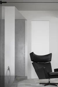 Modern living room featuring a black leather chair and a concrete wall.