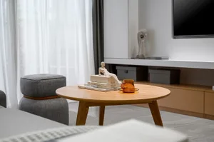 A modern living room featuring wooden coffee table with glass vase, books, and sculpture, upholstered ottoman, and glass vase
