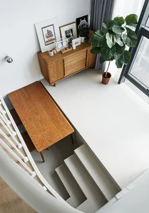 Modern minimalist interior with a wooden staircase, featuring a wooden desk, wooden cabinet, and potted plant under a large w