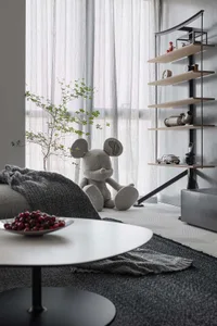 A modern minimalist living room with a small potted plant, a plush Mickey Mouse toy, and a sleek, white coffee table.