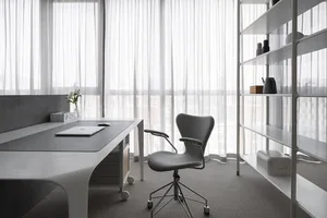 A modern office space with a minimalist design featuring a white desk, gray rolling chair, and white shelves.