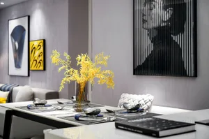 Modern dining room with glass table, golden flowers in a vase, and sleek black and white design.