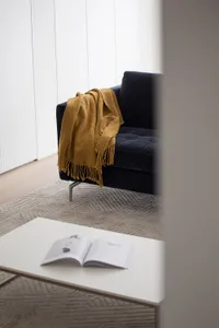 A cozy living room with a dark blue sofa adorned with a mustard yellow blanket and a white coffee table featuring an open boo