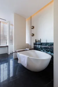 Modern minimalist bathroom featuring a white freestanding bathtub on a black marble floor, with a window allowing natural lig