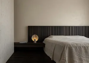 A minimalist bedroom with a wooden headboard and a light-colored bedspread.