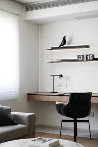 A minimalist home office featuring a wooden desk, black chair, and a black bird sculpture on a floating shelf.