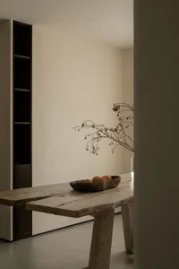 A minimalist interior design featuring a wooden table with fruits and a branch with berries.