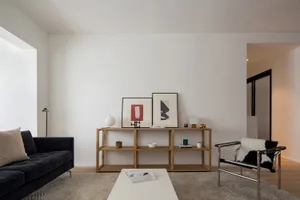 A minimalist living room featuring wooden shelves and a black sofa with white cushions.